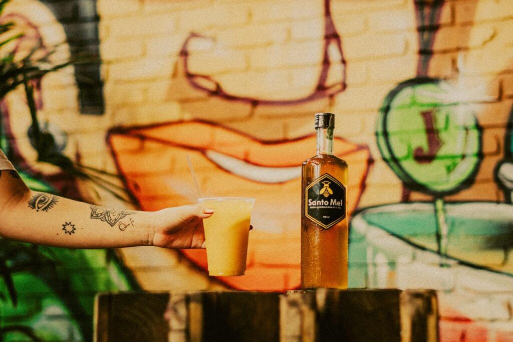 Garrafa e copo da Santo Mel Bebidas servidos em balcão com arte urbana.